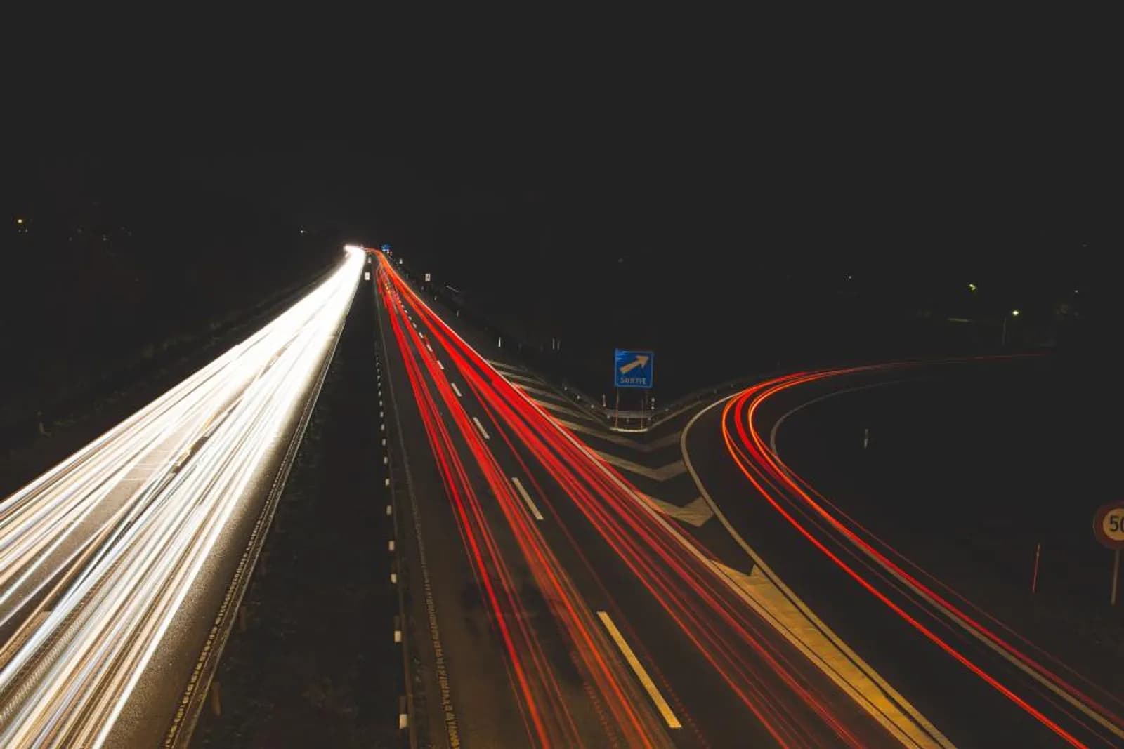 A motorway at night in long exposure, red tail lights running one way and white headlights the other along a single road
